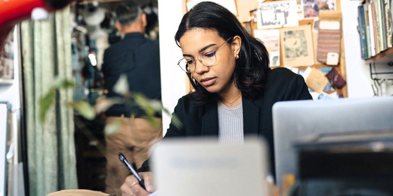 Kvinde arbejder ved computer og tager noter med kuglepen