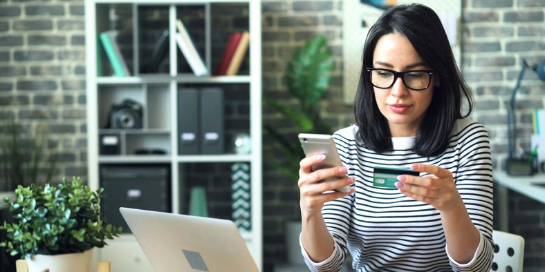 Kvinde med mobiltelefon og betalingskort i hænderne køber ind online